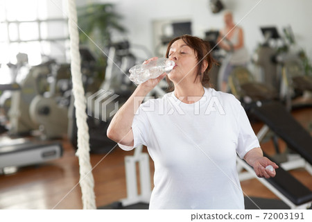 Mature woman drinking water after exercising at gym. Mature woman drinking water after exercising at gym. 72003191