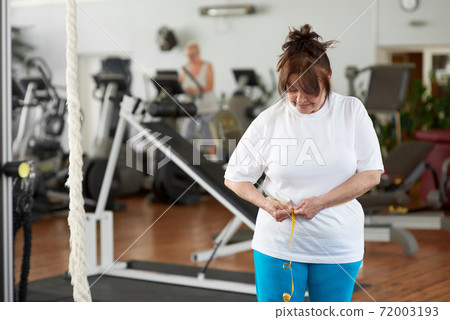 Mature caucasian woman measuring waist in gym. Mature caucasian woman measuring waist in gym. 72003193