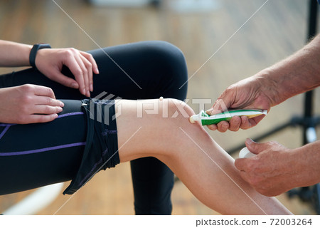Therapist applying ointment cream on female knee. Therapist applying ointment cream on female knee. 72003264