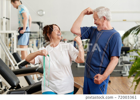 Cheerful senior couple showing their biceps at the gym. Cheerful senior couple showing their biceps at the gym. 72003361