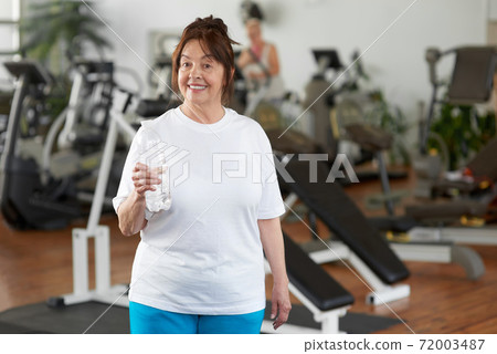 Happy mature woman with water at gym. 72003487