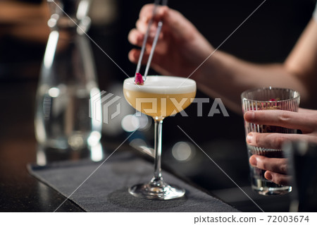 Close-up of a glass with a beautiful delicious cocktail standing on the table in a restaurant. The bartender creates an alcoholic drink for women Close-up of a glass with a beautiful delicious cocktail standing on the table in a restaurant. The bartender creates an alcoholic drink for women 72003674