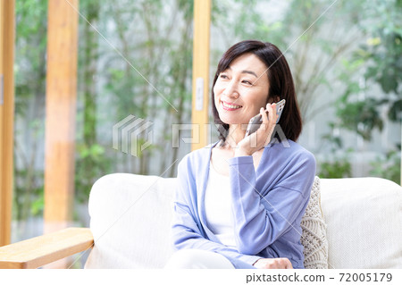 Middle-aged woman calling on her smartphone in the living room Middle-aged woman calling on her smartphone in the living room 72005179