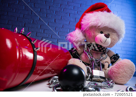 a toy bear in leather belts and a Santa Claus hat in the New year Christmas is chained and handcuffed an accessory for BDSM games next to a fire extinguisher 72005521