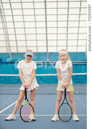 Two active teenage girls in white sportswear standing on tennis field at stadium Two active teenage girls in white sportswear standing on tennis field at stadium 72005887