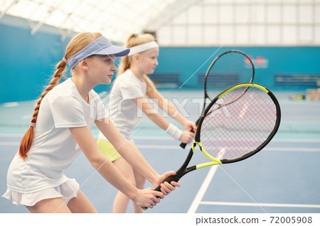 Two teenage girls in activewear standing on stadium with legs bent in knees 72005908