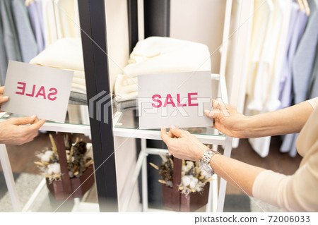 Hands of female shop assistant putting sale card by stack of folded sweaters Hands of female shop assistant putting sale card by stack of folded sweaters 72006033