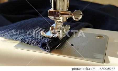 Sewing process on a modern sewing machine, close-up. Sewing machine foot with a needle. Dark blue fabric is trimmed with double wrapping of the fabric edge. Natural sunlight Sewing process on a modern sewing machine, close-up. Sewing machine foot with a needle. Dark blue fabric is trimmed with double wrapping of the fabric edge. Natural sunlight 72006077