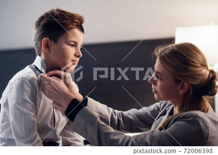 A close up picture of a woman fixing a young boy's tie 72006398