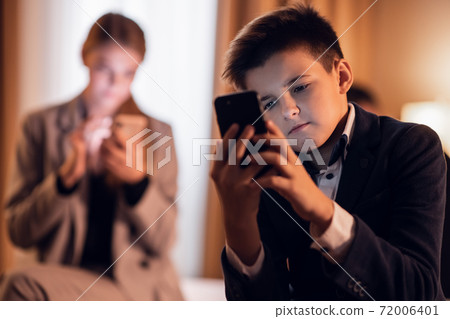A kid sitting and playing on his smartphone, his older sister in 72006401