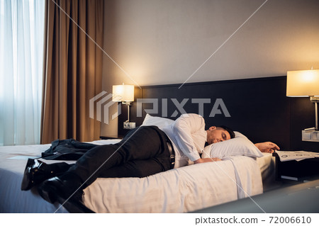 A businessman lying on a bed in a hotel room A businessman lying on a bed in a hotel room 72006610