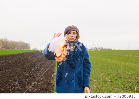 Woman hold burning papers in hand outdoors Woman hold burning papers in hand outdoors 72006913