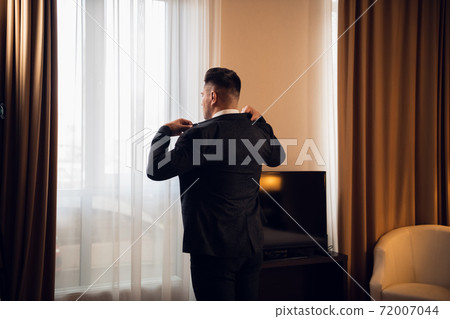 Young handsome businessman adjusting his jacket dressing up at h Young handsome businessman adjusting his jacket dressing up at h 72007044