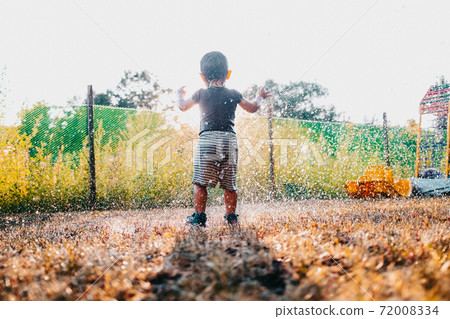Happy adorable toddler boy having fun under rain. Baby laughs, he is very glad weather. 72008334