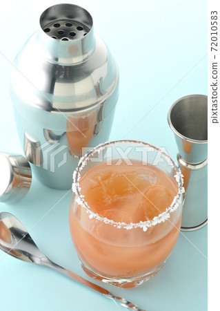 Pink salty dog with salt on the edge of the glass, cocktail shaker and major cup 72010583