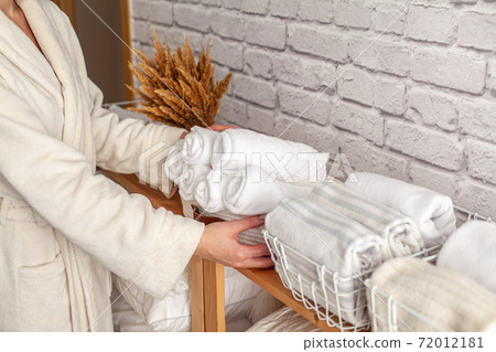Woman in warm bathrobe is placing basket of rolled cotton bath towels on wooden shelf Woman in warm bathrobe is placing basket of rolled cotton bath towels on wooden shelf 72012181