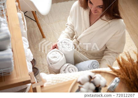 Young woman in warm robe is organizing linen closet with neatly folded towels, sheets and blankets. Young woman in warm robe is organizing linen closet with neatly folded towels, sheets and blankets. 72012207