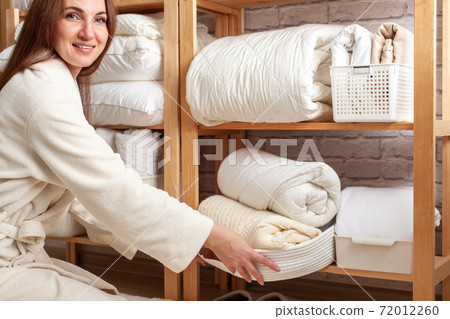 Young woman in warm robe is organizing linen closet with neatly folded towels, sheets and blankets. Young woman in warm robe is organizing linen closet with neatly folded towels, sheets and blankets. 72012260