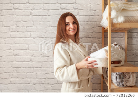Young woman in warm robe is organizing linen closet with neatly folded towels, sheets and blankets. Young woman in warm robe is organizing linen closet with neatly folded towels, sheets and blankets. 72012266