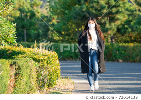 A woman wearing a mask and taking a walk in the park A woman wearing a mask and taking a walk in the park 72014139