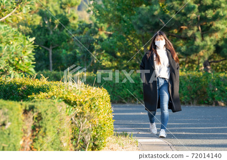A woman wearing a mask and taking a walk in the park A woman wearing a mask and taking a walk in the park 72014140