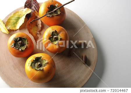 Photographed persimmons, acorns and fallen leaves on a log cutting board on a white background (overhead view) 72014467