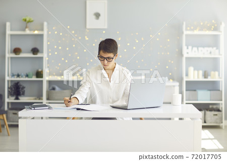 Serious young woman focusing on work or study sitting at desk with laptop at home Serious young woman focusing on work or study sitting at desk with laptop at home 72017705