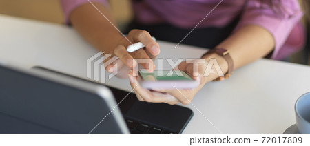 Female hands using smartphone while working with tablet on worktable Female hands using smartphone while working with tablet on worktable 72017809