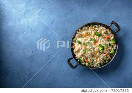 Vegan rice with fried vegetables, broccoli, green peas and carrots, top shot on a blue background Vegan rice with fried vegetables, broccoli, green peas and carrots, top shot on a blue background 72017825