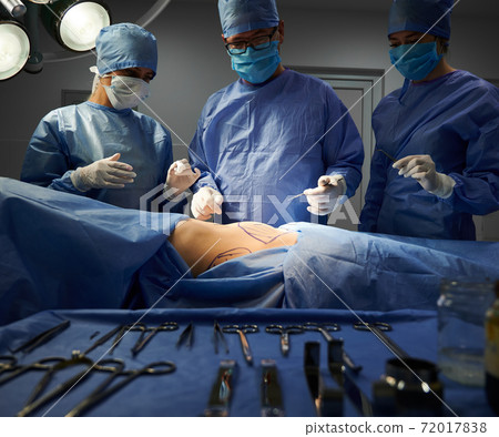 Surgical team standing beside patient in operating room. Surgical team standing beside patient in operating room. 72017838