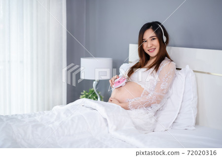 pregnant woman listening to fetal heart sound through headphones on bed pregnant woman listening to fetal heart sound through headphones on bed 72020316