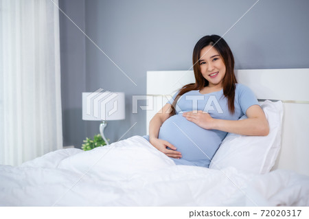 happy pregnant woman stroking her belly on bed happy pregnant woman stroking her belly on bed 72020317