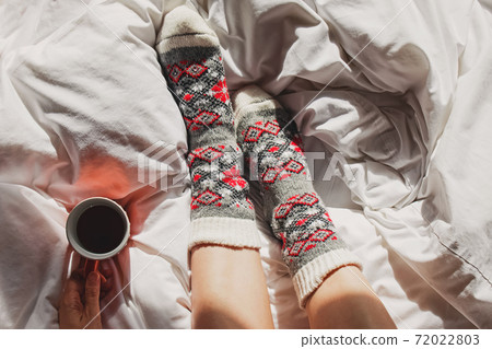 A cup of coffee or tea and female feet in warm knitted socks A cup of coffee or tea and female feet in warm knitted socks 72022803