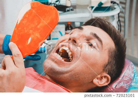 The patient at the dentist,a man holds a mirror in his hands, assesses the condition of his teeth. 72023101