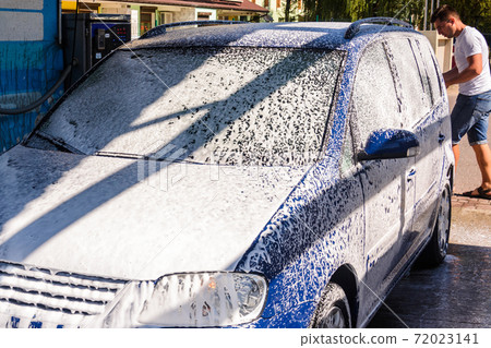 Car wash, a person at a self-service car wash, under a stream of pressure puts foam on the car. 72023141