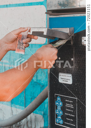 A man at a car wash, a man shoves money into a self-service machine to wash his car. 72023151