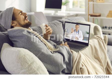 Sick man coughing and sneezing while having online medical consultation with eHealth doctor 72023344