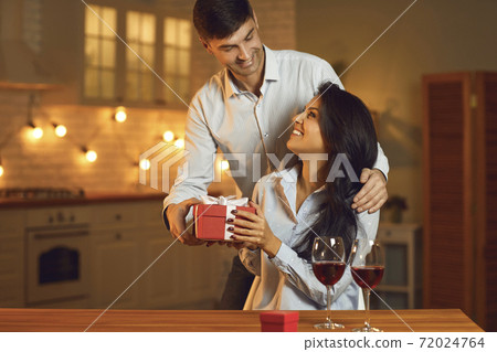Smiling young man giving red gift box present for his pretty girlfriend during Valentines day celebration Smiling young man giving red gift box present for his pretty girlfriend during Valentines day celebration 72024764