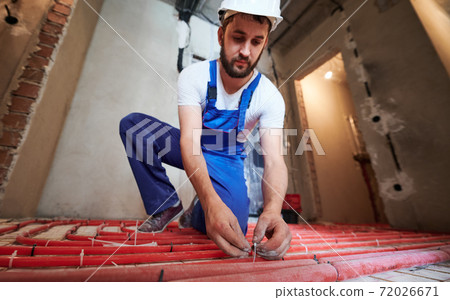 Male plumber installing underfloor heating pipes. Male plumber installing underfloor heating pipes. 72026671