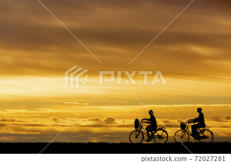 Silhouettes of men and women who go to school by bicycle against the setting sun 72027281