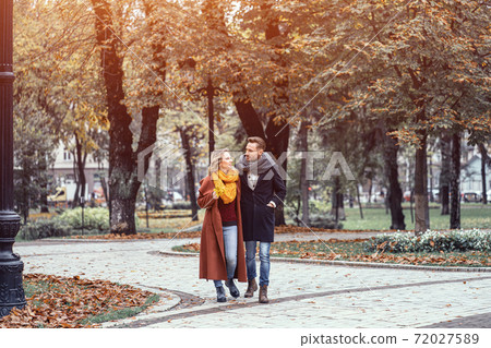 A married couple is walking in the autumn park with a cute hug. Outdoor shot of a young couple in love walking along a path through a autumn park. Tinted image 72027589