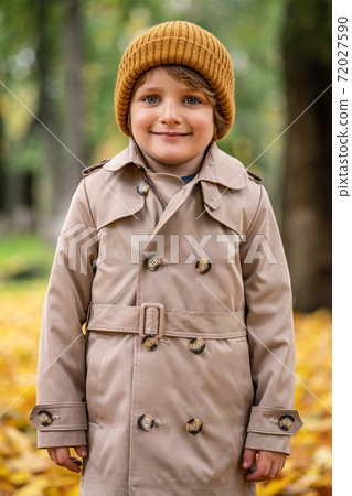 A cute little boy in an autumn coat and a hat is standing on the autumn street and smiling cutely at the camera. Tinted image A cute little boy in an autumn coat and a hat is standing on the autumn street and smiling cutely at the camera. Tinted image 72027590