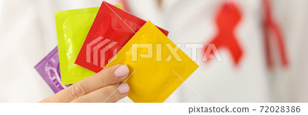 Infectious disease doctor with red ribbon on uniform holds lot of condoms in hand closeup Infectious disease doctor with red ribbon on uniform holds lot of condoms in hand closeup 72028386