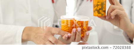 Doctors with red ribbon on uniforms are holding jars of medicines closeup Doctors with red ribbon on uniforms are holding jars of medicines closeup 72028388