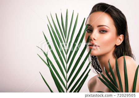 Young beautiful woman with green leaves near face and body. Skin care beauty treatments concept.  Closeup girl's face with green leave. White model with clean, health skin of face - posing at studio 72029505
