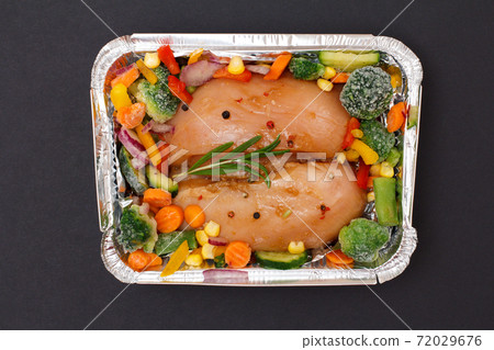 Raw chicken breasts or fillet in metal container with vegetables on black background. Raw chicken breasts or fillet in metal container with vegetables on black background. 72029676