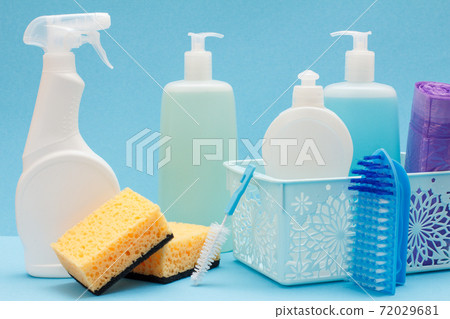Bottles of dishwashing liquid in basket, sponges and brushes on blue background. Bottles of dishwashing liquid in basket, sponges and brushes on blue background. 72029681