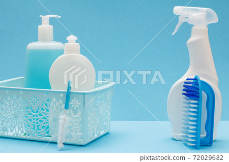Bottles of dishwashing liquid in basket and brushes on blue background. Bottles of dishwashing liquid in basket and brushes on blue background. 72029682