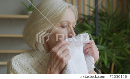 An elderly woman sniffs a fresh towel at home 72030126