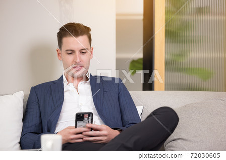 Business man with suitcase using smartphone app sit on sofa Business man with suitcase using smartphone app sit on sofa 72030605